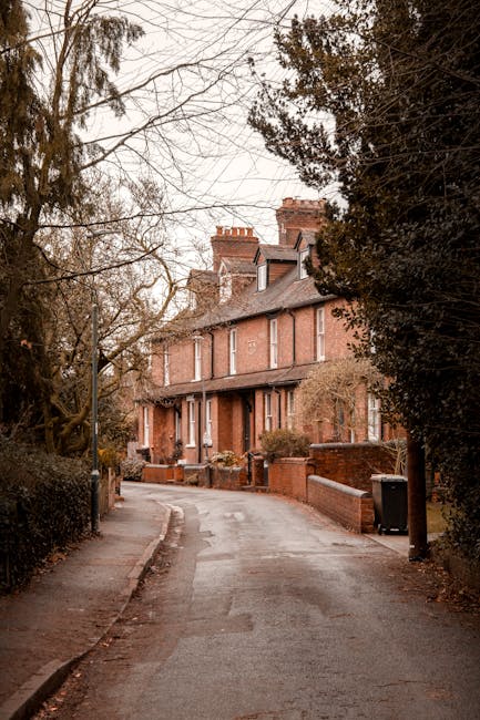A narrow residential street in Belsize Park lined with traditional brick-built terraced houses featuring pitched roofs and chimneys. The pavement runs along the left side, bordered by a low brick wall